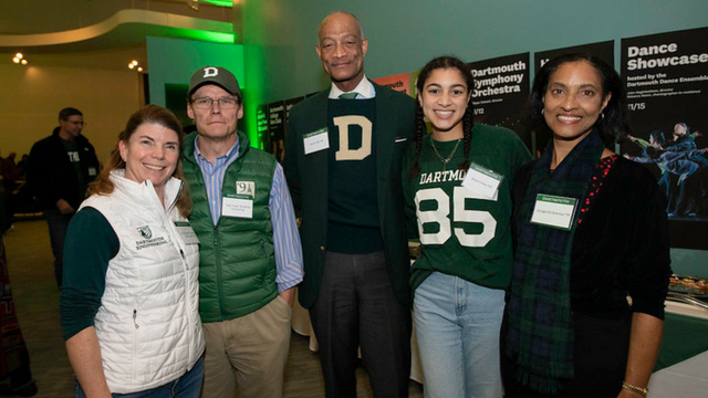 Five people wearing Dartmouth gear with arms around each other posing for a photo. 