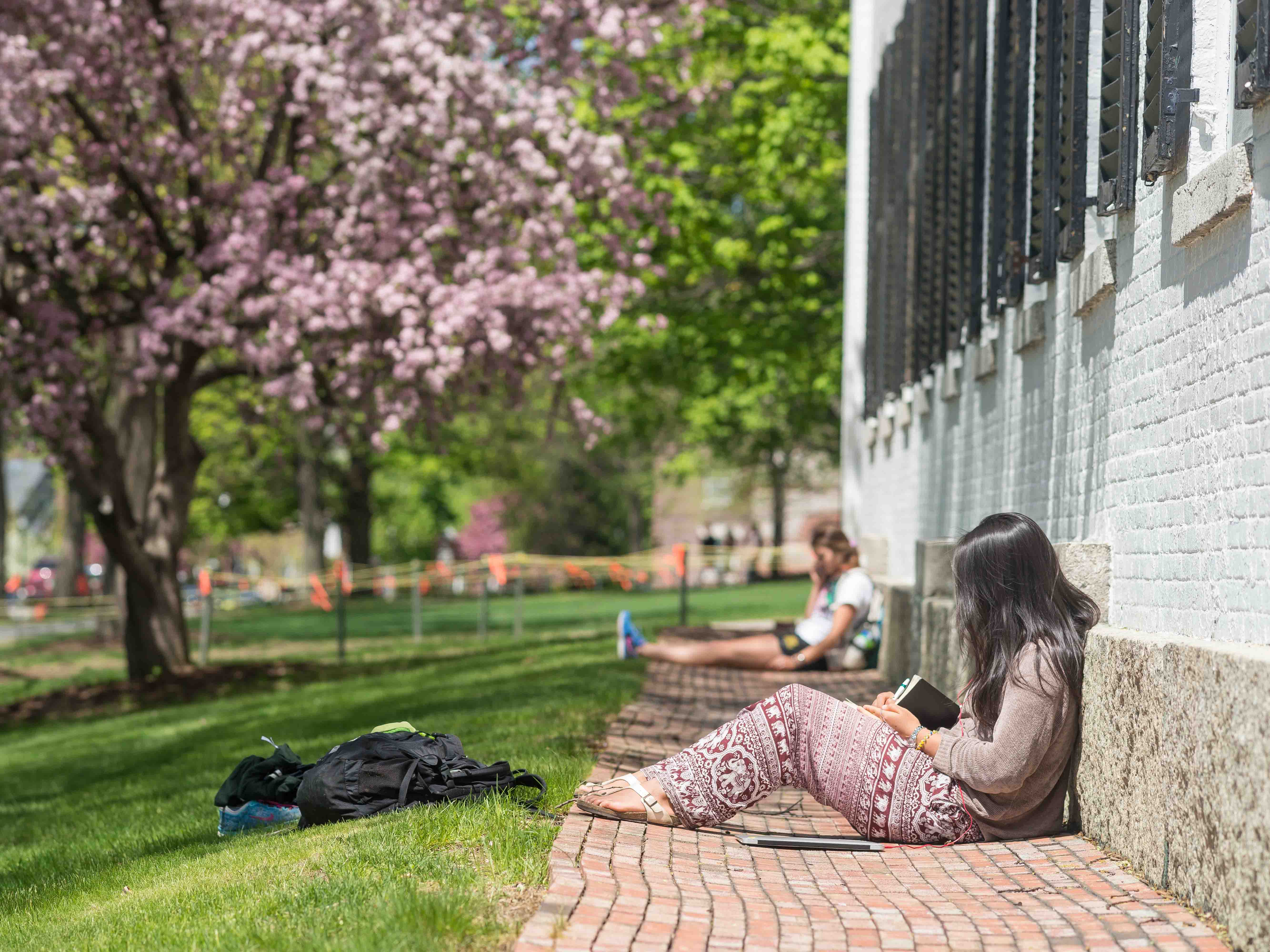 An exterior view of two students seated along the wall of Dartmouth Hall