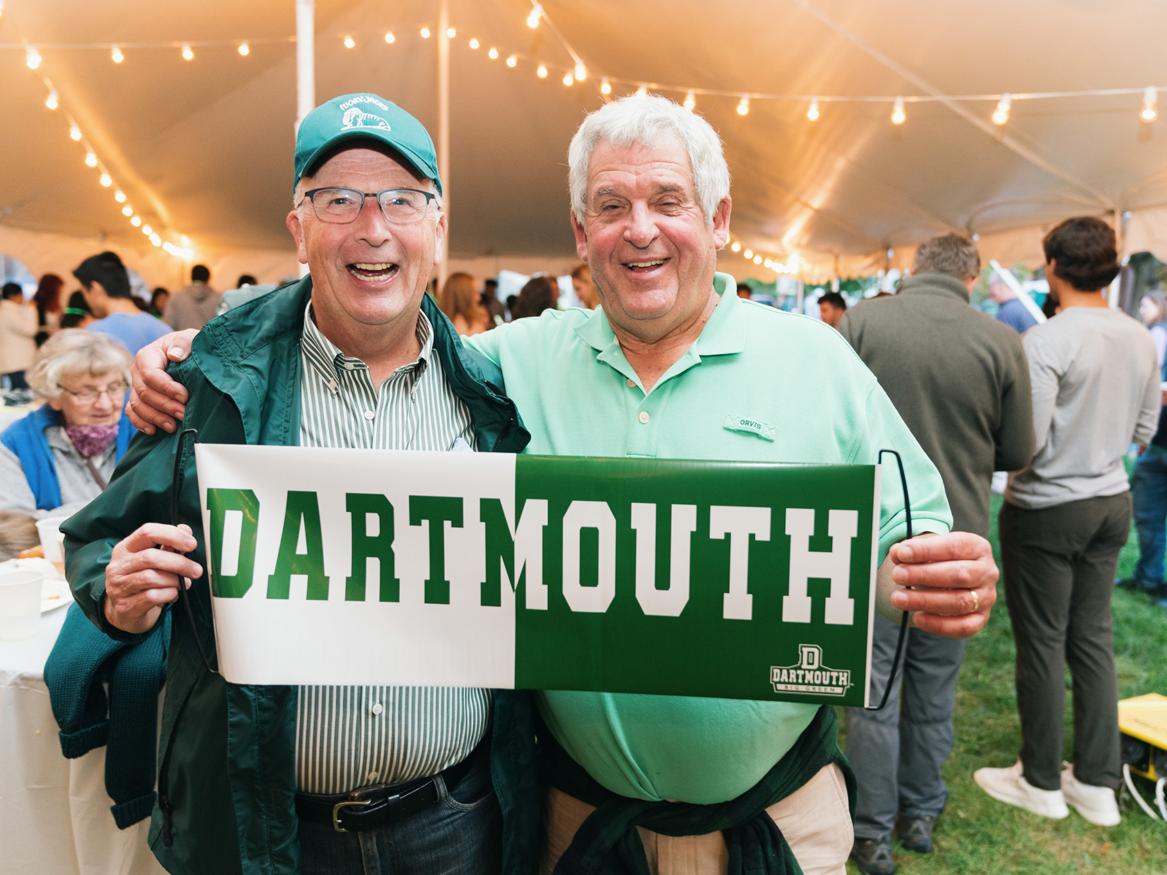 two men hold a Dartmouth banner in a tent at a campus event
