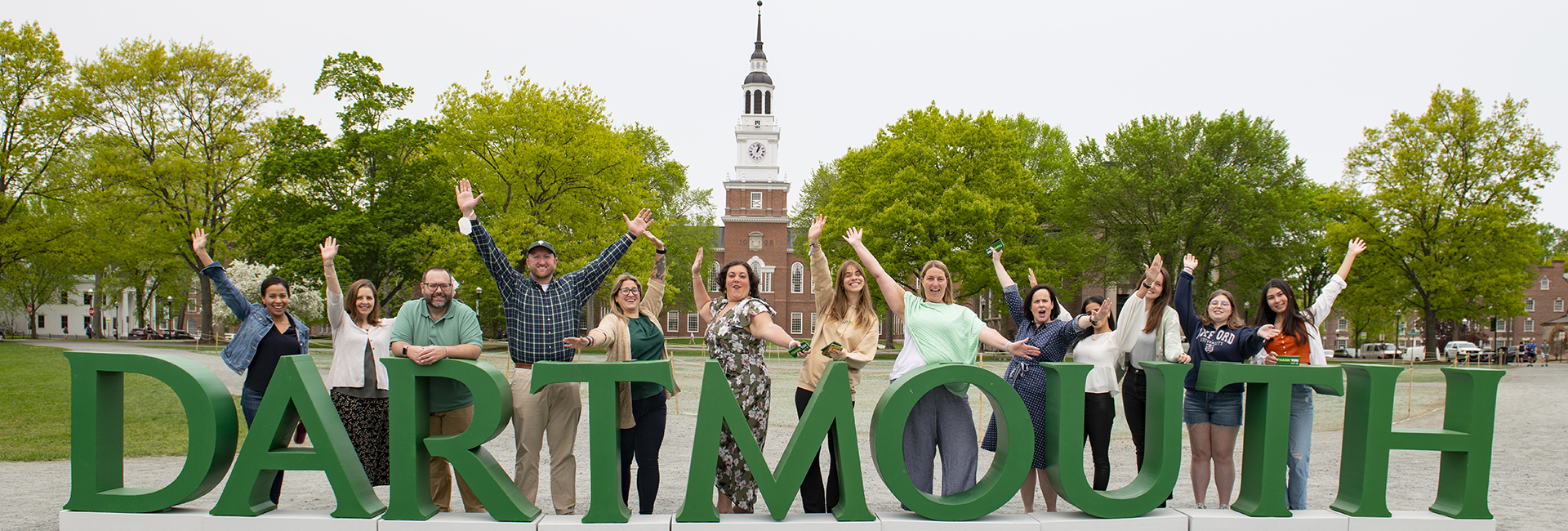 Dartmouth Alumni Relations staff standing behind the Dartmouth letters on the Dartmouth Green with Baker Tower in the background