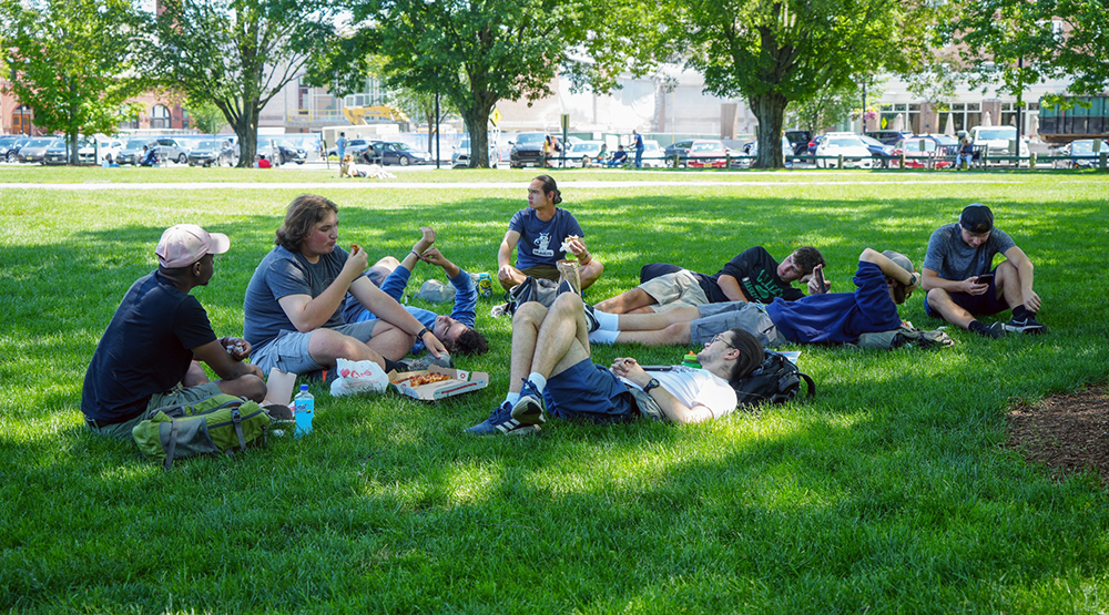 Several students sit on the Dartmouth green on a warm spring day