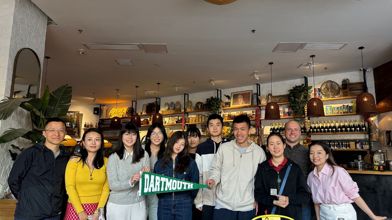 A group of students posing together in a restaurant. One student holds a Dartmouth pennant. 
