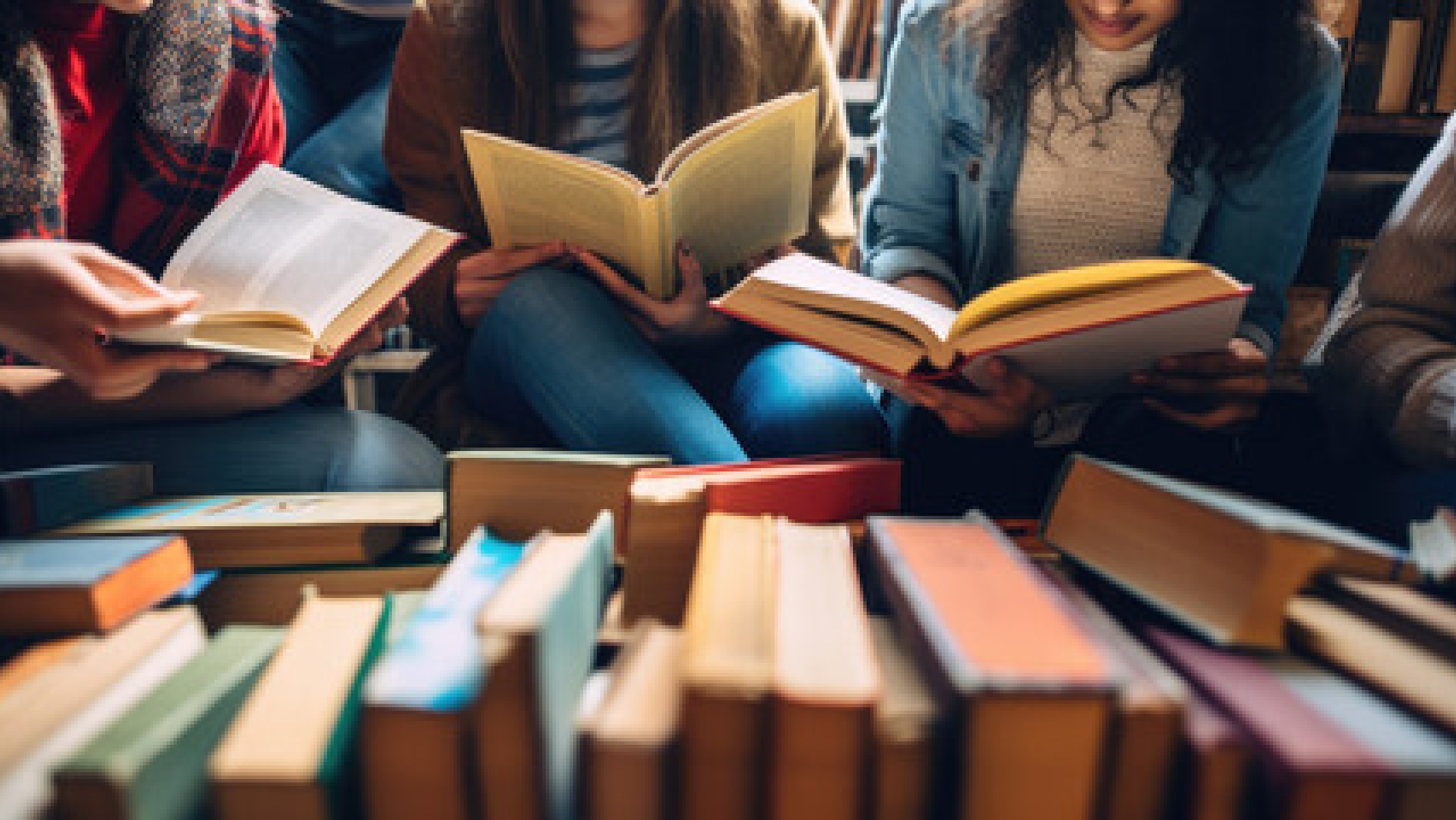 A photo of a group of people holding open books in front of a full table of books. 