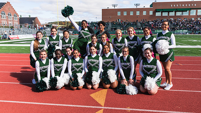 The cheer team poses for a photo on the sidelines of a Dartmouth football game