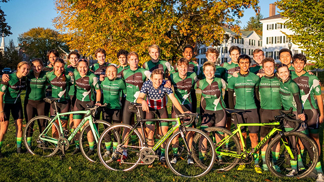 The cycling team poses on the green with their bikes at sunset on an early fall day
