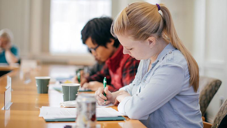 Two students writing notes at a desk during class