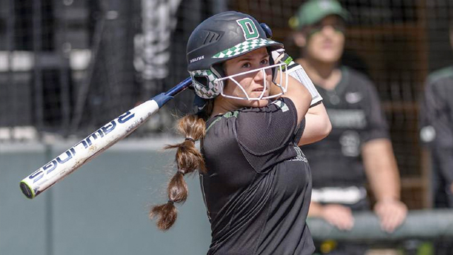 A Dartmouth softball player post swing watches the ball fly through the air