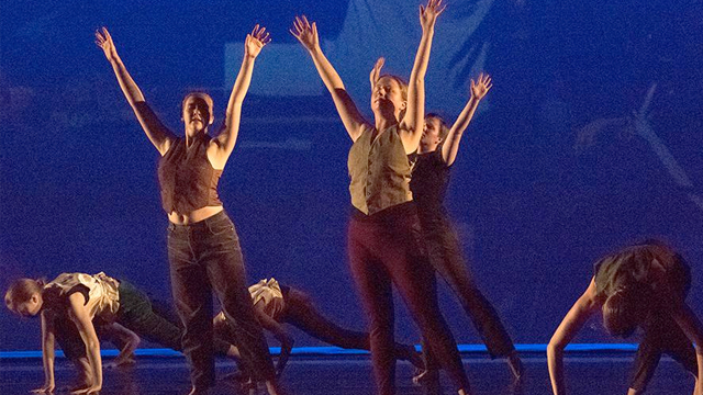 Three dancers raise their hands in the air as they perform on stage at Dartmouth