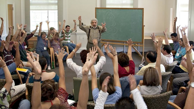 John Rassias teaches before a large classroom of students with their hands raised
