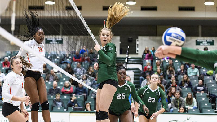 A Dartmouth volleyball player jumps as the ball passes her and a teammate returns the ball 
