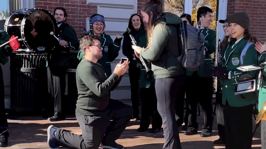 Gui Marinho ’22 bends down on one knee to propose to Laurel Semprebon Marinho ’22 in the middle of their band performance at Homecoming