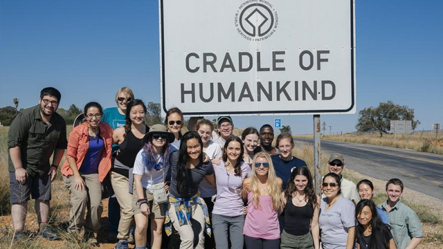 A large group of students gather in front of the sign that reads "Cradle of Humankind" in South Africa