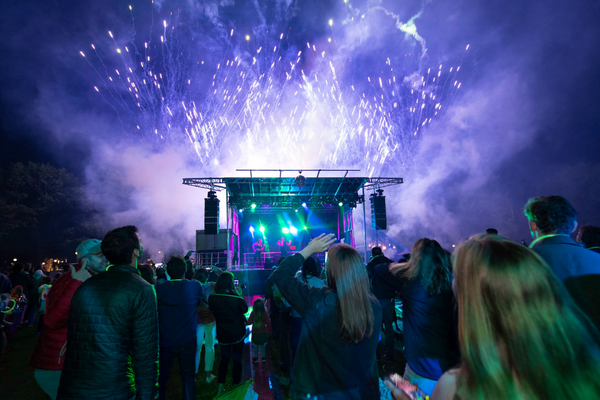 An image of people partying outdoors on the Green looking at a stage performance with pyrotechnics.
