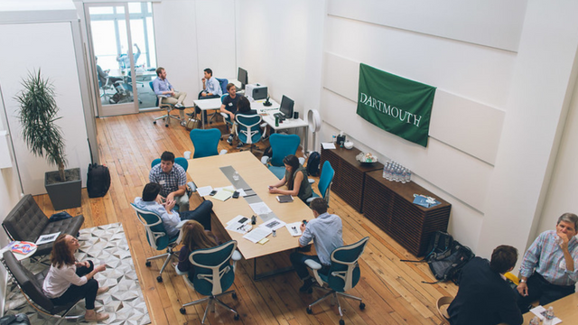 A group of entrepreneurs collaborating in a conference room with a green Dartmouth banner on the wall. 