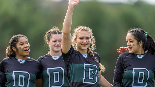 A photo of four women's rugby players smiling, one with her right arm in the air. 
