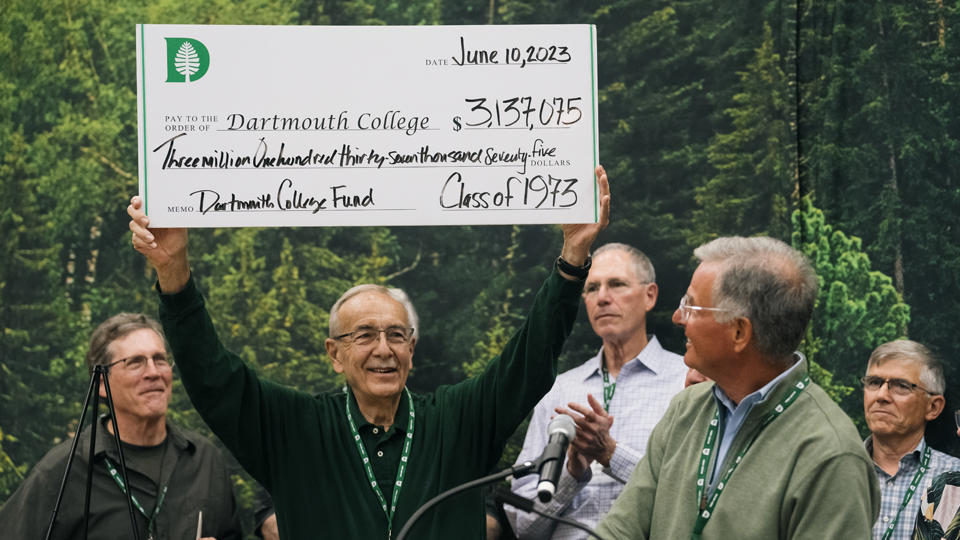 Class of 1977 member holding a large check over his head