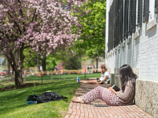 Girl leaning up against Dartmouth Hall studying on sunny day