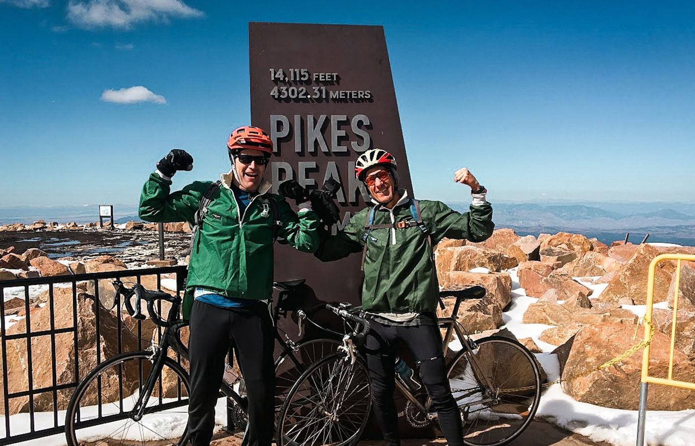 Two alums flexing their muscles with their bikes at the top of Pikes Peak