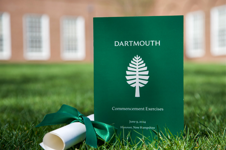 A green commencement program sitting on the grass in front of Baker. 