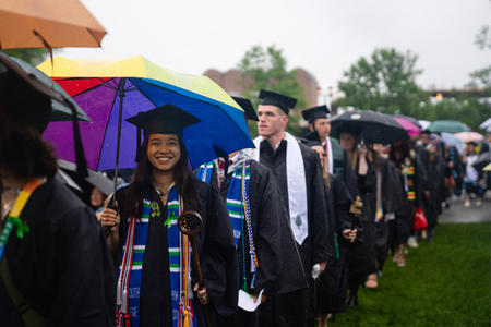 Graduates wearing cap and gown carrying umbrellas. 