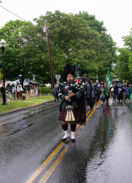 Bagpiper leading commencement procession walking on rainy pavement