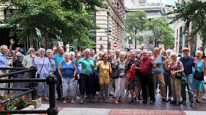 A group of Osher attendees waving in a group photo on a trip to Boston