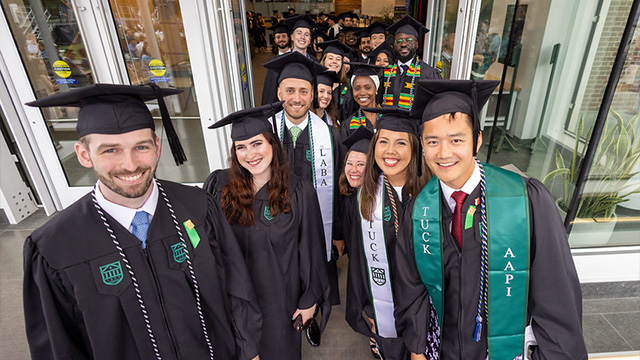 A group of 2024 graduates smiling for a photo dressed in their caps and gowns on Commencement day.