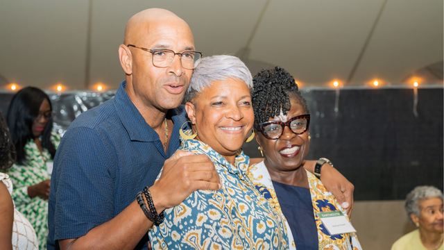 Three people posing and smiling at the camera underneath a tent with lights. 