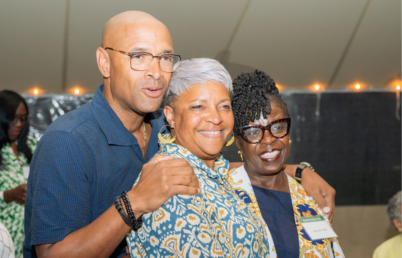 Three people posing and smiling at the camera underneath a tent with lights. 