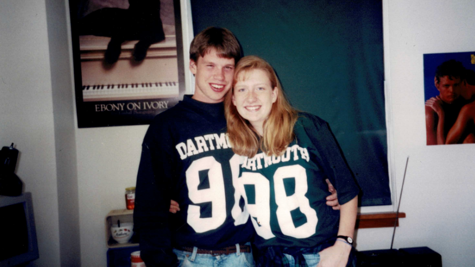 Two students posing together with arms around in each other. They are both wearing their Dartmouth 98 long sleeved class T shirts. 