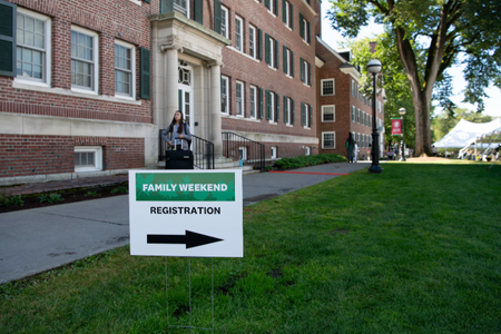 A lawn sign for family weekend registration in front of a residence hall. 