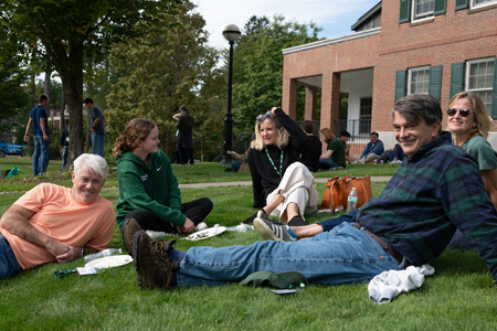 Parents and sutdents lounging on the grass on campus. 