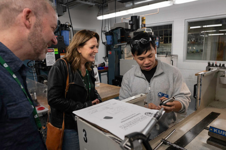 A student doing a technology demonstration for two onlooking parents. 