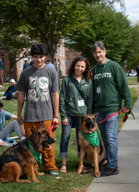 A family in Dartmouth gear posing with two german shepherds wearing green bandanas. 