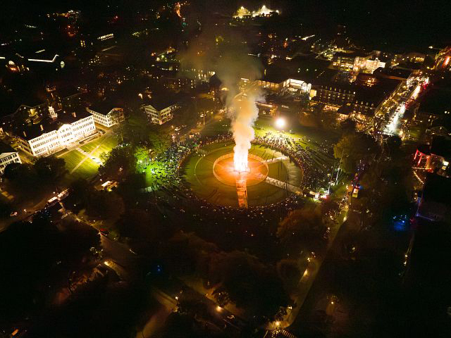 An aerial shot of the Homecoming bonfire lit up on the Green with spectators gathered around. 