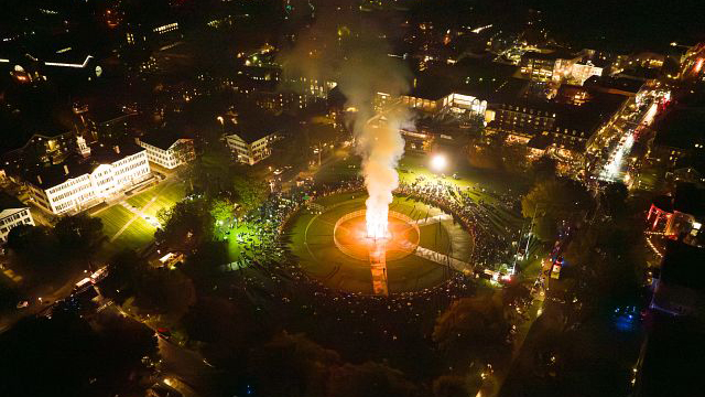 An aerial shot of the Homecoming bonfire lit up on the Green with spectators gathered around. 