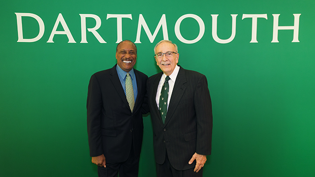 A photo of Tyrone Byrd posing for a photo in front of a green background with the word Dartmouth on it. 