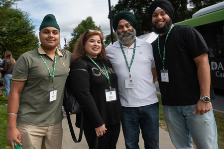 A family posing with four people wearing their green weekend lanyards on a sidewalk. Three people are wearing turbans. 