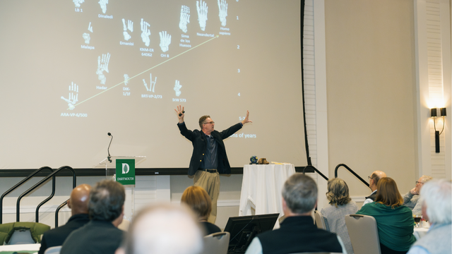 Professor of Anthropology Jerry DeSilva giving a presentation, his arms outstretched as he speaks.