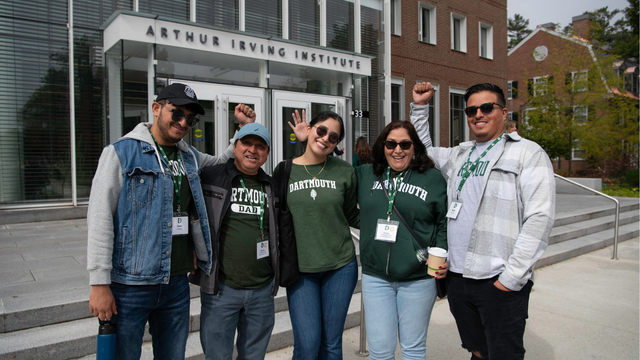 A family wearing Dartmouth gear posing in front of the Irving Institute building