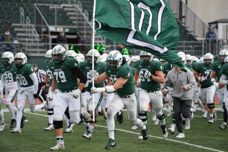 The Dartmouth football team taking the field with their green D flag. 