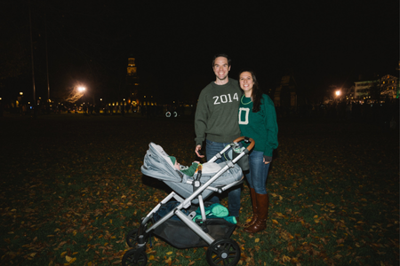 An alum couple in Dartmouth gear posing with their baby in a stroller. 