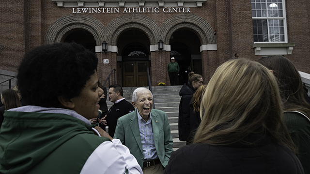 A photo of Stephen Lewinstein, joyfully smiling and laughing in front of the newly renamed Lewinstein Athletic Center