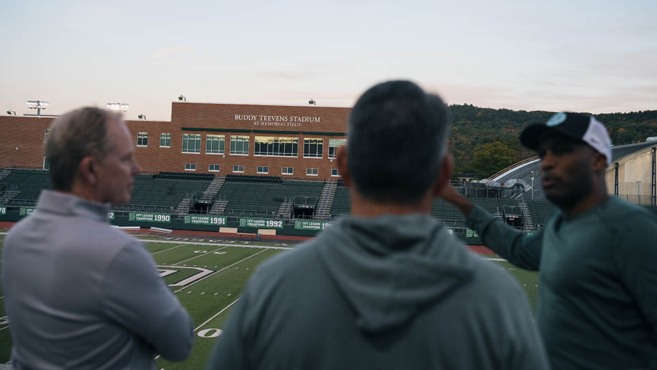 Three attendees at the dedication of Buddy Teevens stadium look across the stands to the newly reveal sign that displays Buddy Teevens Stadium