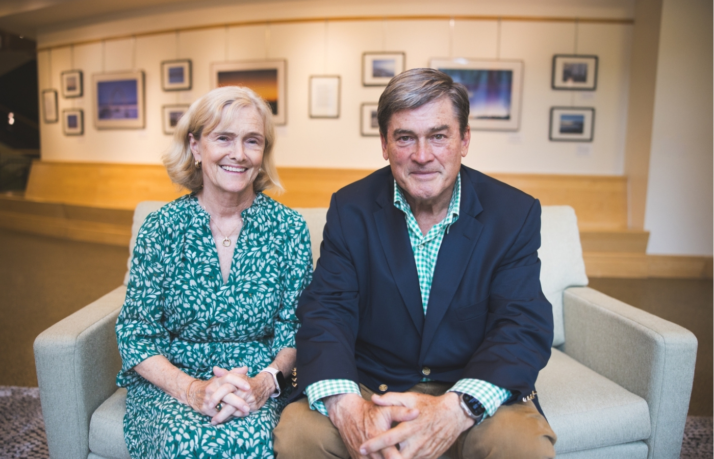 Tom and Gina Russo seated on a sofa in front of a gallery wall. 