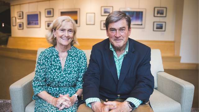 Tom and Gina Russo seated on a sofa in front of a gallery wall. 