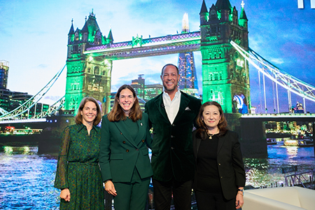 Dartmouth trustee Jane Pfaff Novak, Ric Lewis, and Susan Huang stand with President Beilock on stage in front of the Tower Bridge lit green