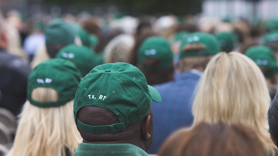 A group of people wearing hat that say "Tx, BT" at a memorial service honoring the late Buddy Teevens, who frequently signed emails with the letters. 