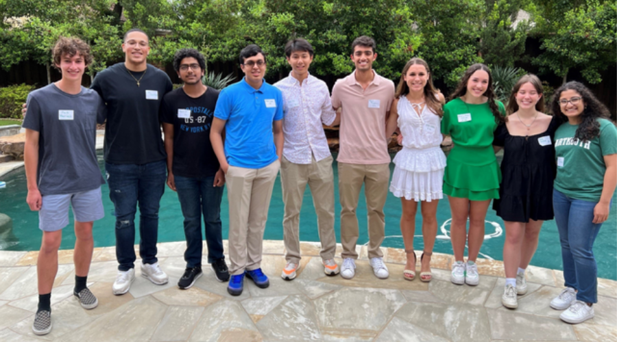 A group of students and young alumni posing by a swimming pool at an event.