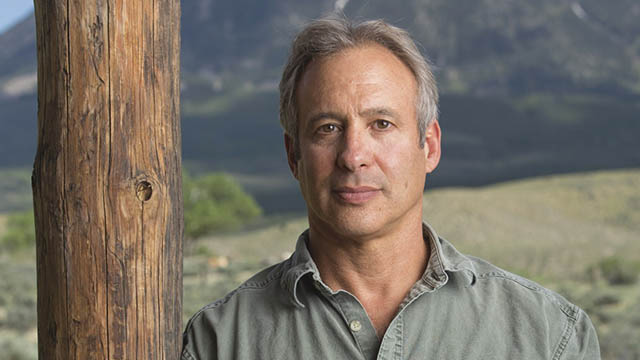 A portrait of Peter Heller standing with a mountain in the background